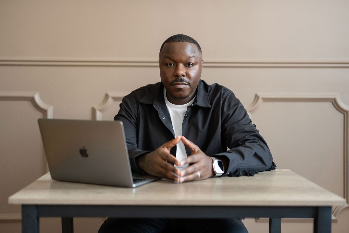 Jamel Lewis Sr. at a table with his laptop, hands together, looking at the camera